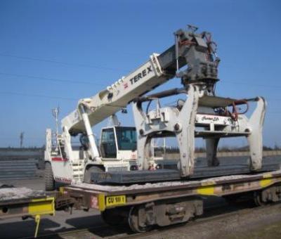 White automatic billet tong crane.attachment placing a slab of metal down on a trailer.